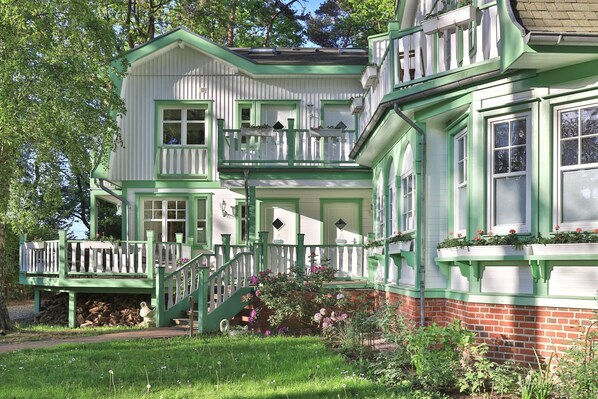 A two-story house with a green and white exterior, a front porch with a staircase, and a brick foundation.
