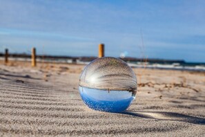 Une sphère de verre transparente sur une plage de sable, avec une clôture en bois et l’océan en arrière-plan.