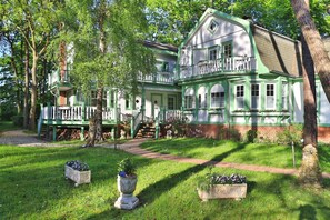 A large, two-story house with a green and white exterior, a balcony, and a well-maintained garden with flower beds.