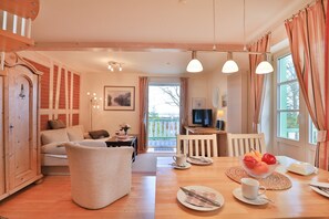 A cozy living room with a sofa, a dining table with plates and cups, a TV, and a balcony view.