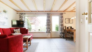 En stue med en rød sofa, et fjernsyn, et spiseområde med bord og stole, samt et stort vindue med gardiner.