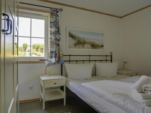 A bedroom with a bed, a nightstand, a bedside table, a window with curtains, and a painting on the wall.