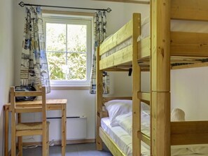 A room with two bunk beds, a wooden desk, and a chair.
