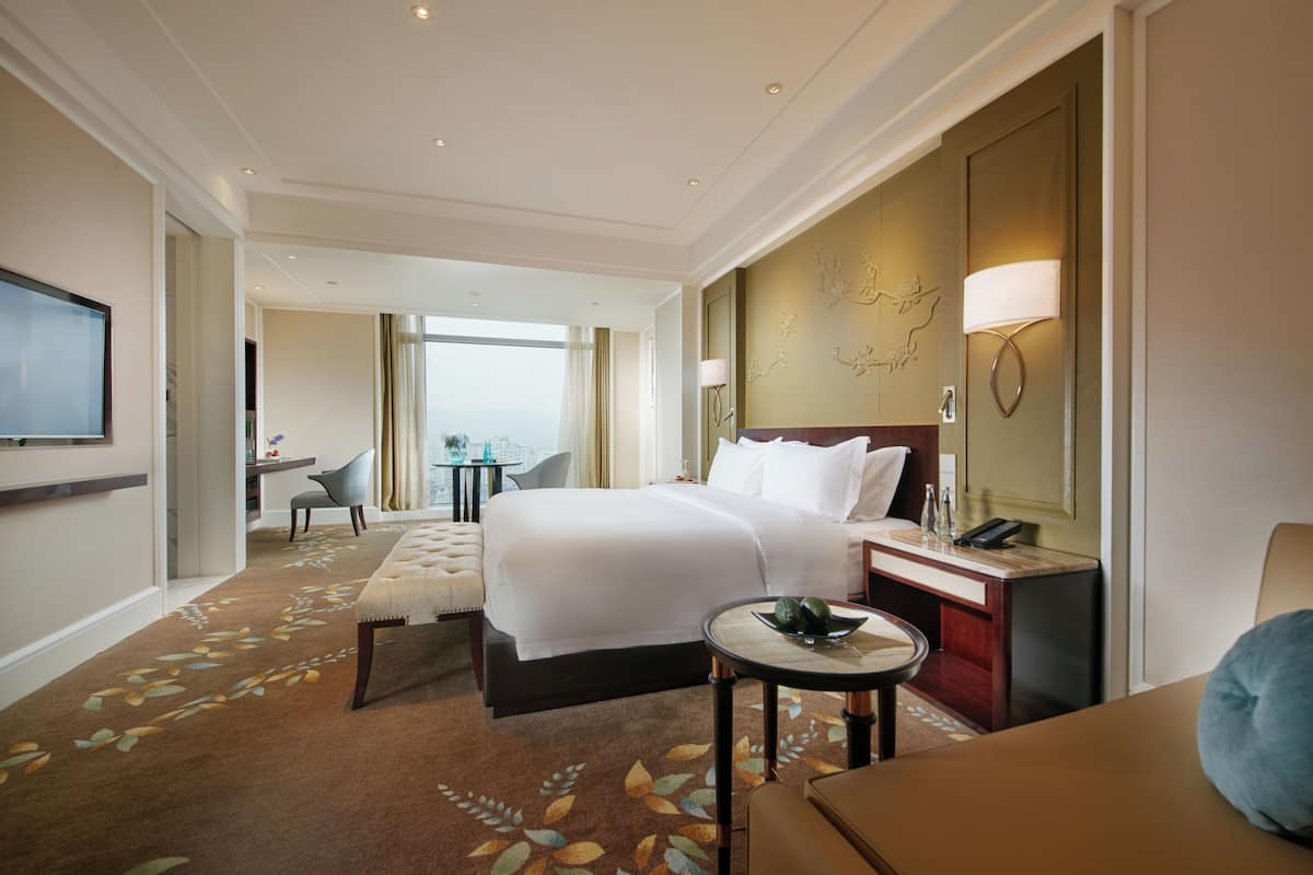 Ein Hotelzimmer mit einem großen Bett, einem Schreibtisch, einem Stuhl, einem Fernseher und Blick auf die Stadt.