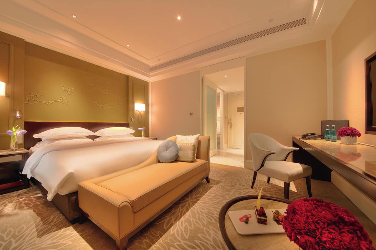 Ein Hotelzimmer mit einem großen Bett, einem Schlafsofa, einem Schreibtisch mit Stuhl und einem durchgehenden Türspalte sichtbaren Badezimmer.