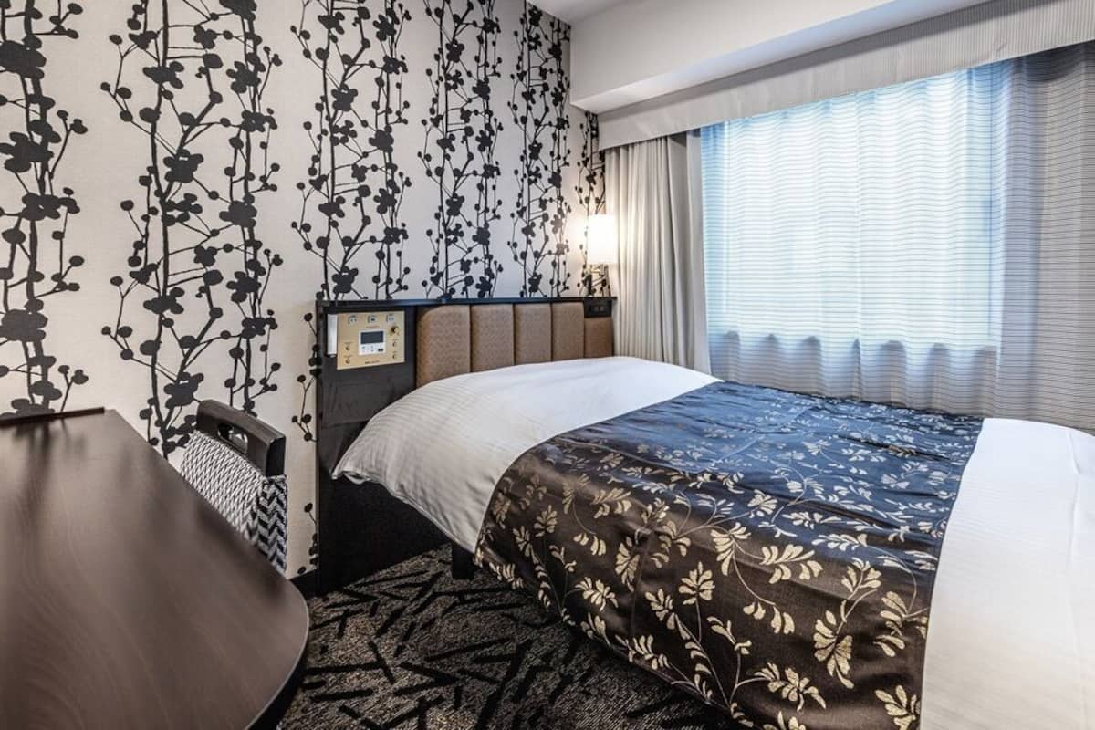 Ein Hotelzimmer mit Bett, Schreibtisch, Nachttisch und einem Fenster mit Vorhängen.