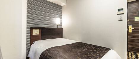 A hotel room with a bed, a headboard with a patterned design, a bedside lamp, and a door with a lock.