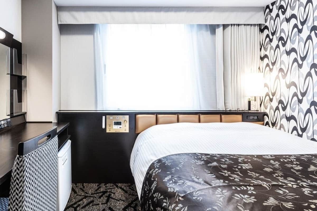 A hotel room with a bed, a desk, a mirror, and a window with curtains.