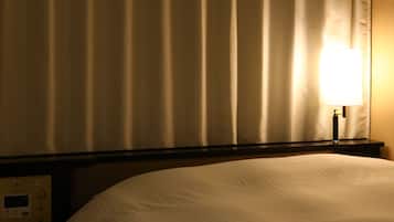 A hotel room with a bed, a nightstand with a control panel, and a lamp.