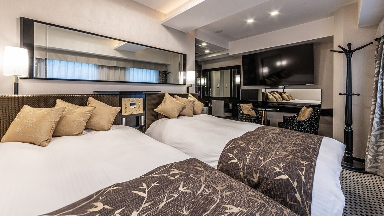 A hotel room with two beds, a TV, a desk, and a chair.