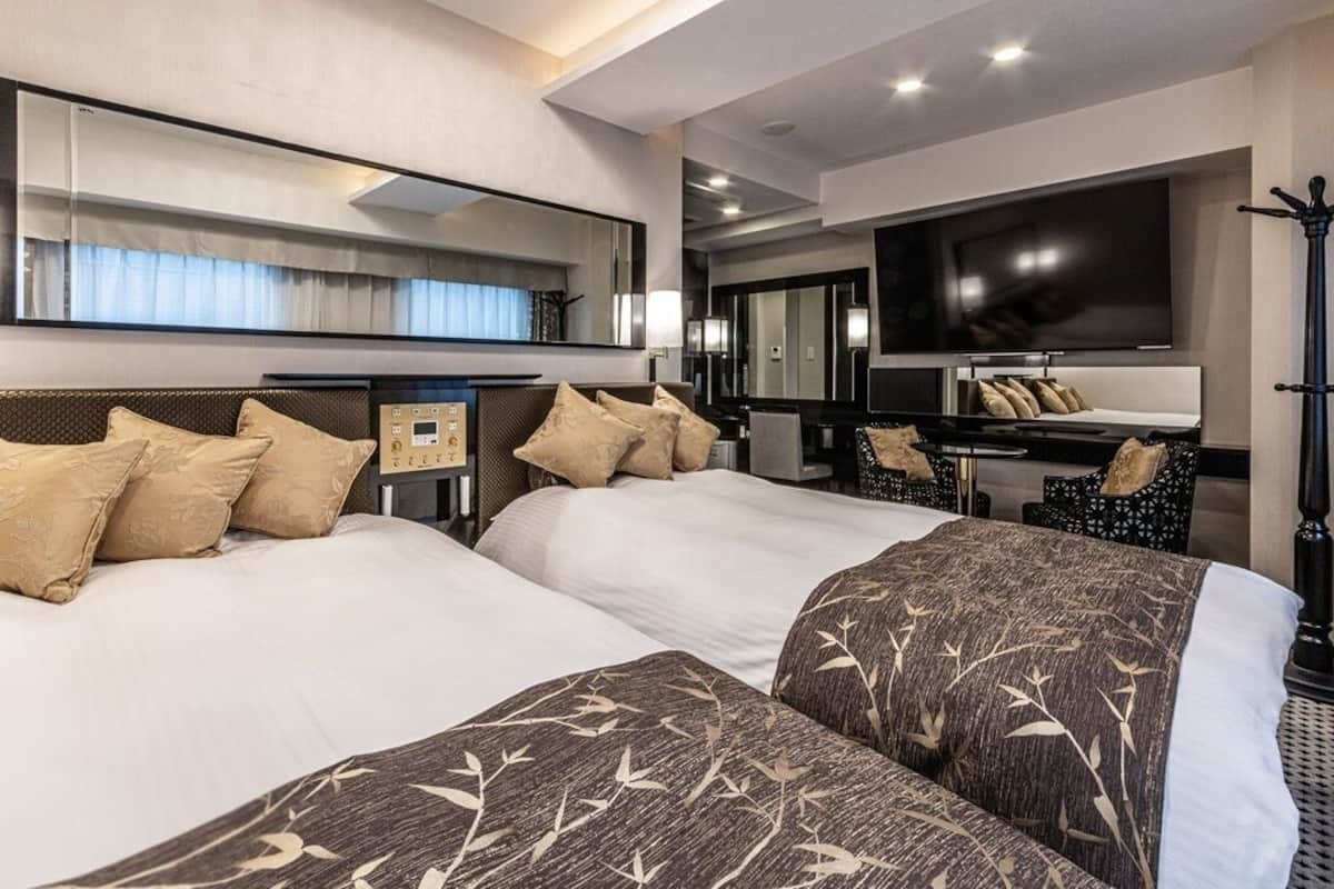 A hotel room with two beds, a TV, a desk, and a chair.