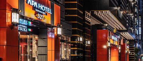 A modern hotel with a prominent 'APHA HOTEL' sign, featuring a number '327' and a 'KROPONGI SUIX' sign below. The building has a contemporary design with orange and black accents and a brick facade.