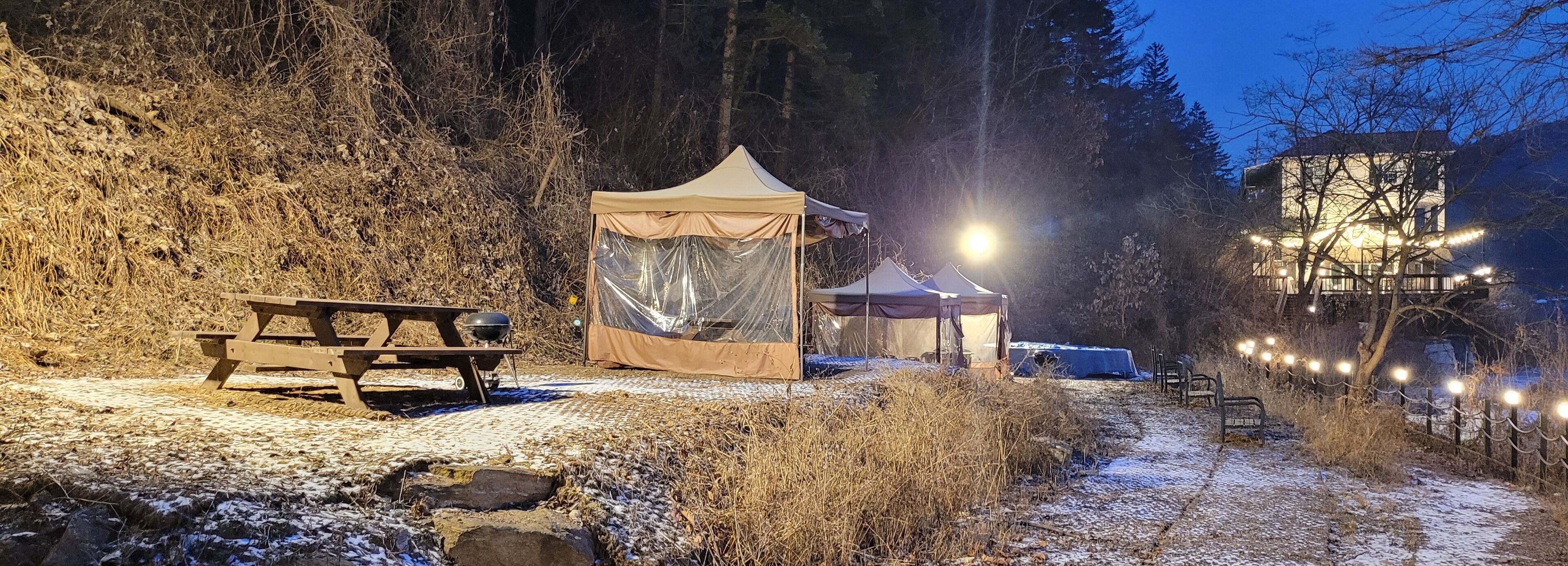 A campsite with a tent, picnic table, and a building with lights.