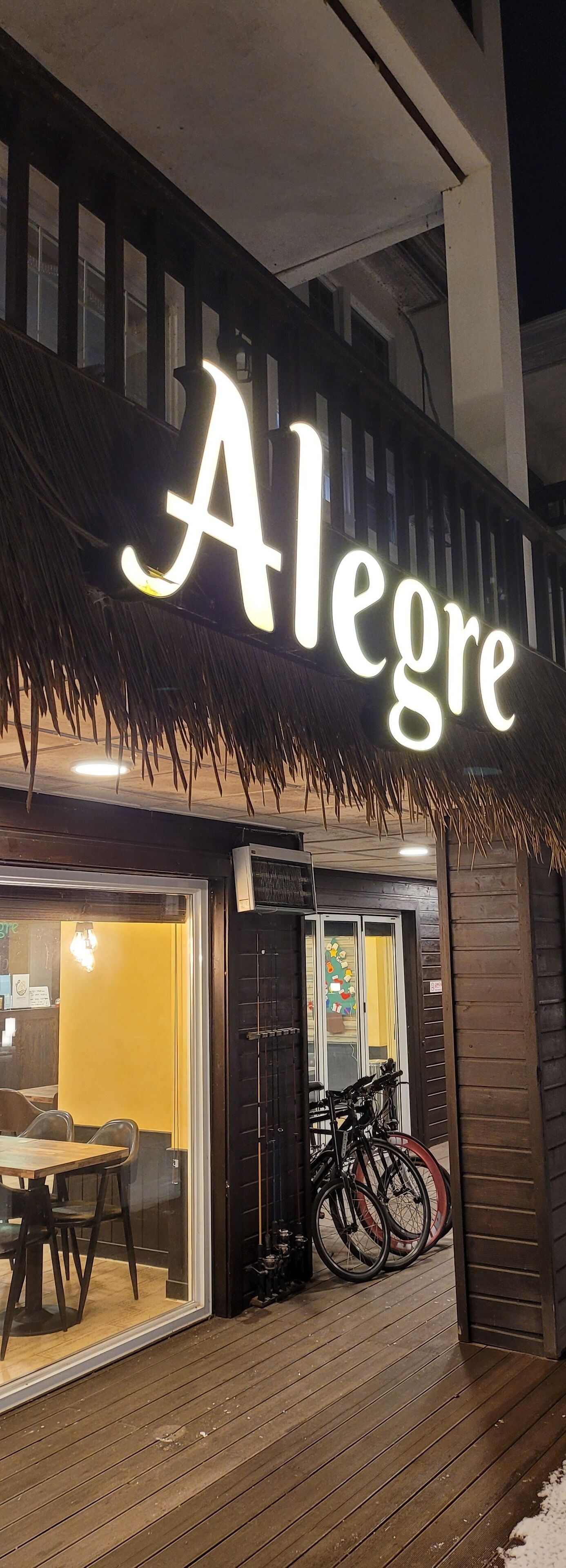 A restaurant named "Alegre" with a thatched roof entrance, visible seating area with tables and chairs, and bicycles parked outside.