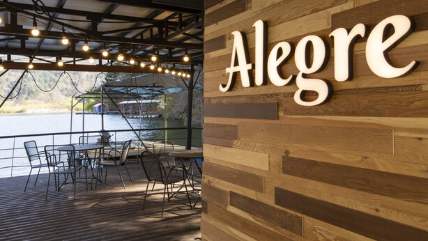 Pared de madera con el nombre 'Alegre' y una zona de terraza con mesas y sillas.