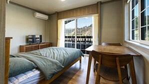 Un dormitorio con una cama, una mesa de madera, una silla, un televisor y un ventanal corredizo que da a un balcón.