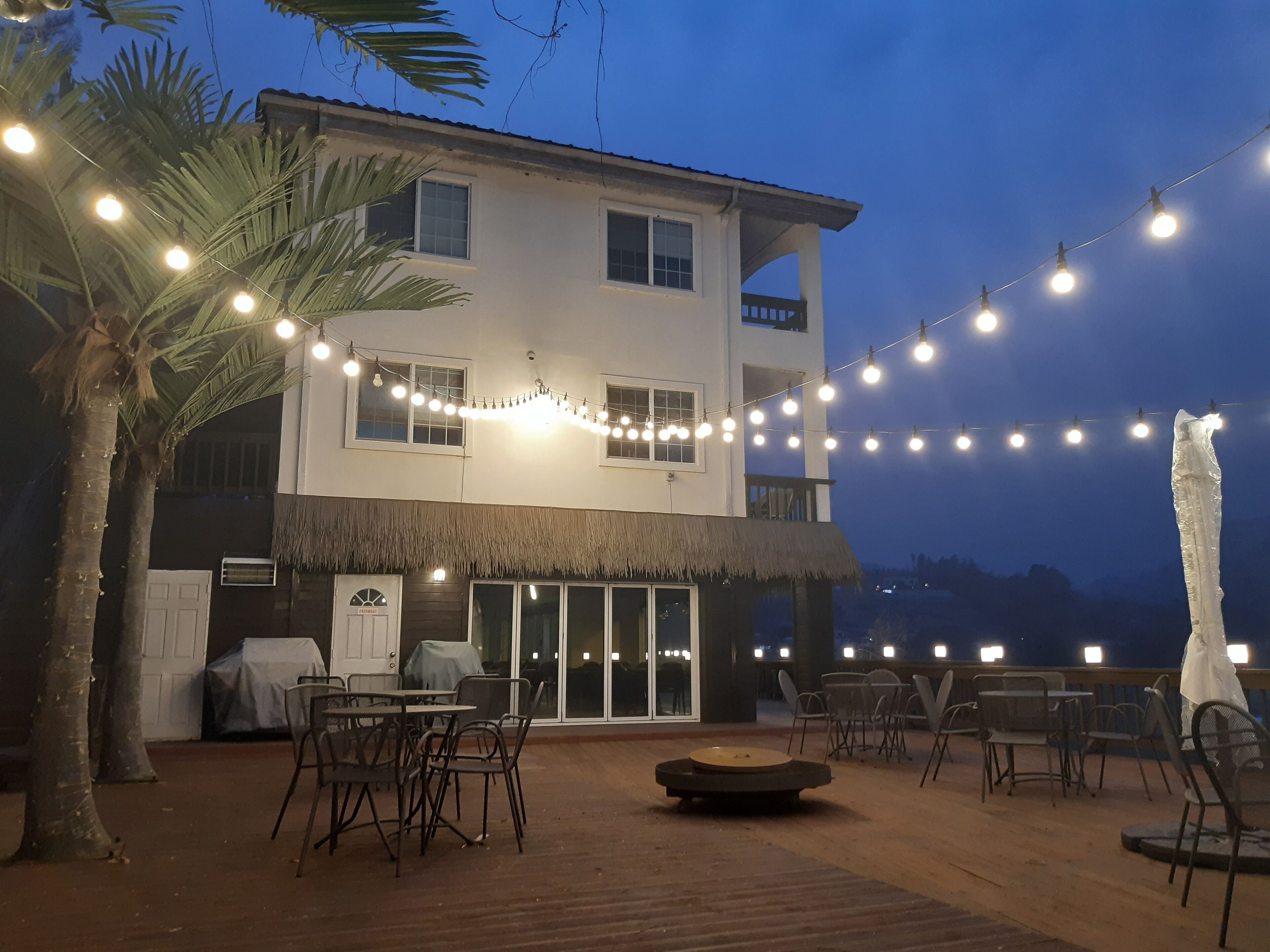 A two-story building with a thatched-roof patio area, string lights, and outdoor seating.