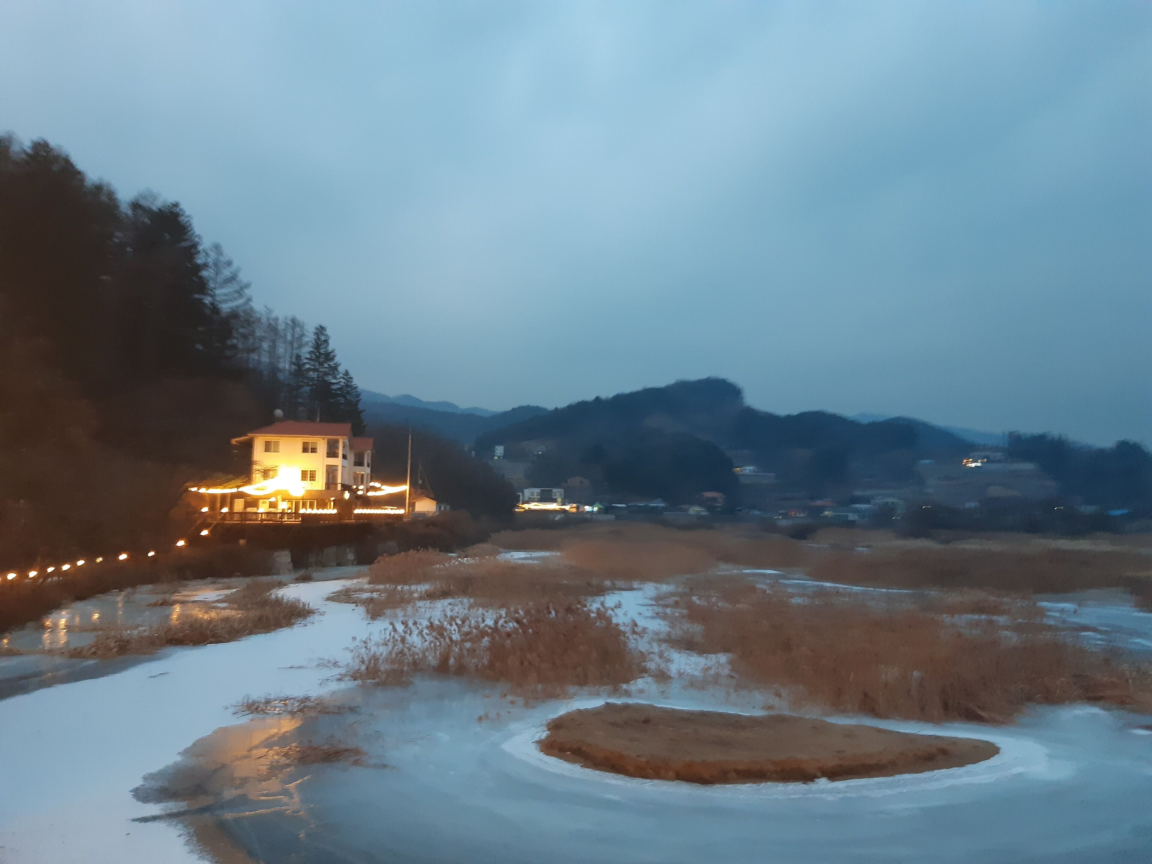 Uma casa com varanda, cercada por neve e um rio.