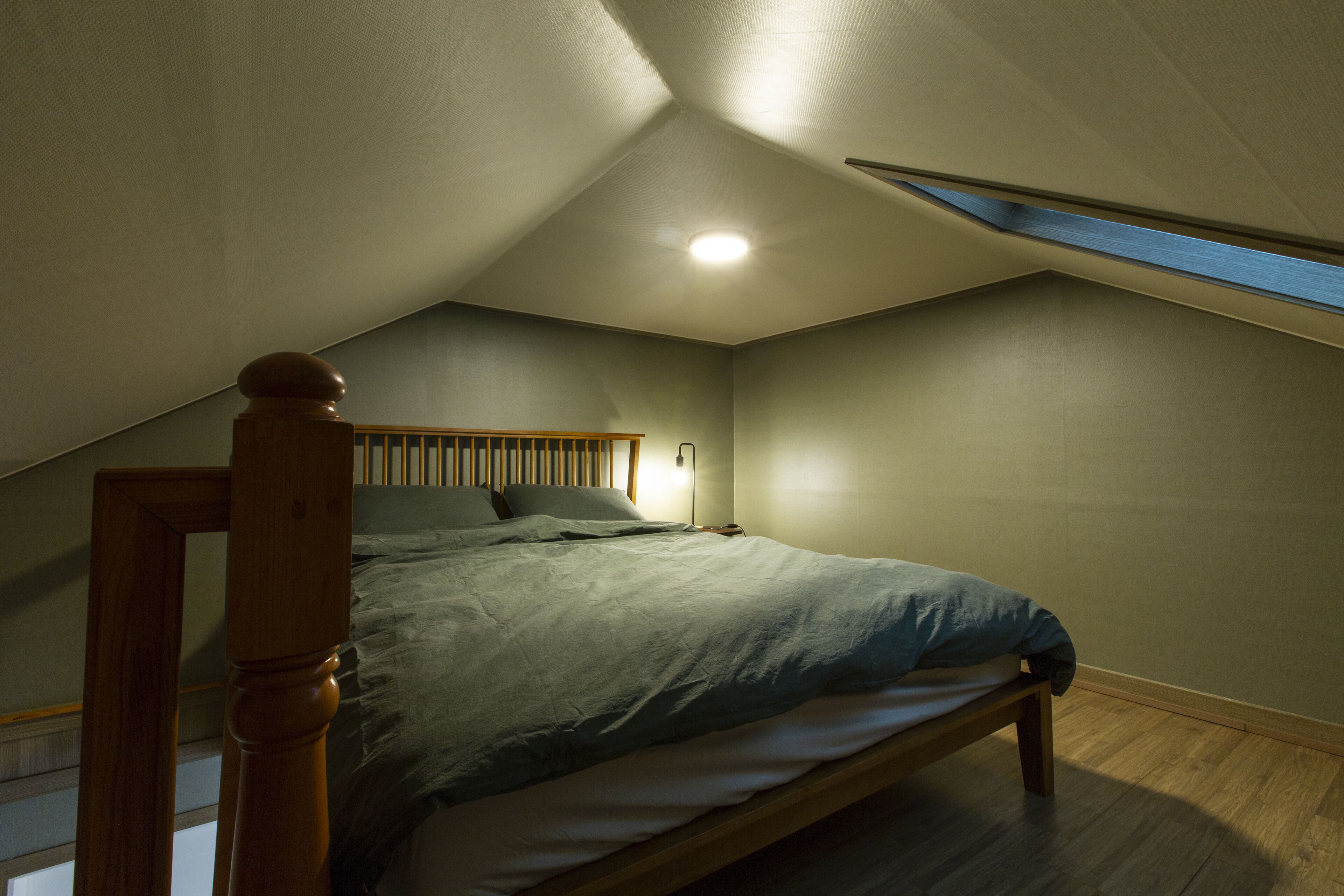 Una camera da letto con soffitto spiovente, un lucernario, un letto con testiera in legno e un comodino.