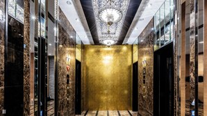 A modern elevator lobby with marble walls, a gold finish on the walls, and a reflective floor. - Apa Hotel Higashi Shinjuku Kabukicho Tower (Tokyo)