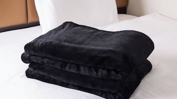 A neatly folded black blanket on a bed with white sheets and a white pillow.