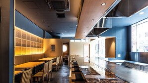A modern restaurant with a long counter, wooden chairs, and a marble floor. - Apa Hotel Higashi Shinjuku Kabukicho Tower (Tokyo)