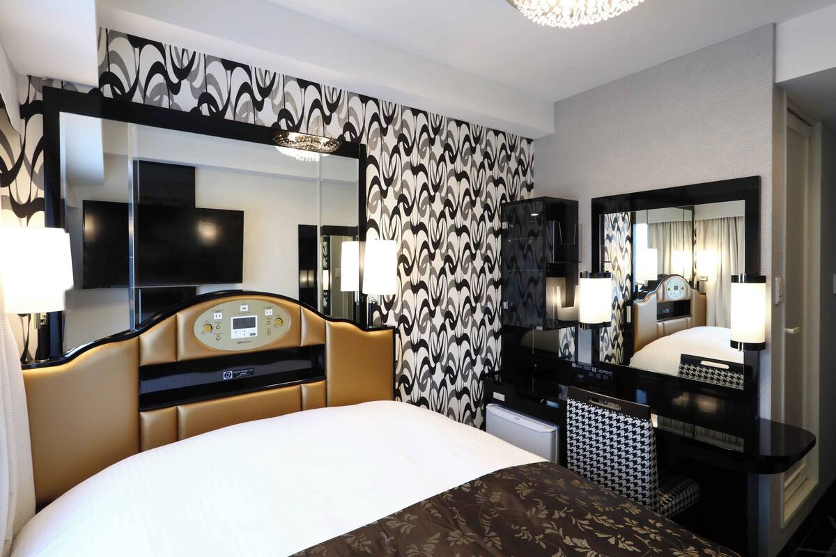 A hotel room with a bed, a desk with a computer, a TV, and a large mirror.