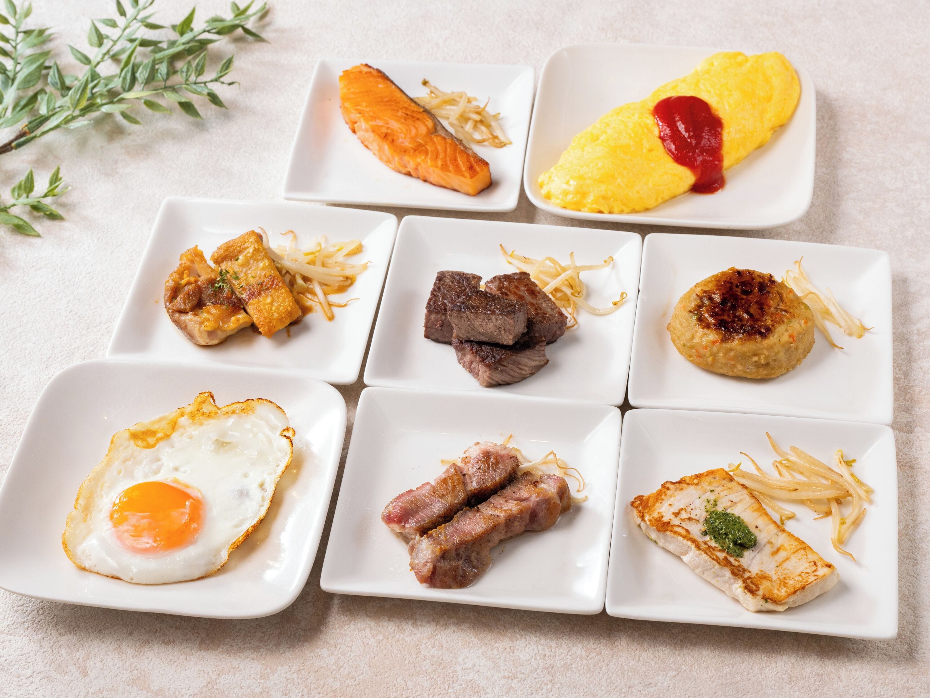 Variedad de platos que incluyen salmón, bistec y un huevo frito, dispuestos sobre platos blancos cuadrados.
