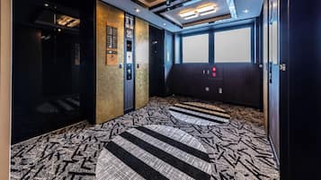 Interior de un ascensor con alfombra estampada, controles en la pared e iluminación empotrada en el techo.