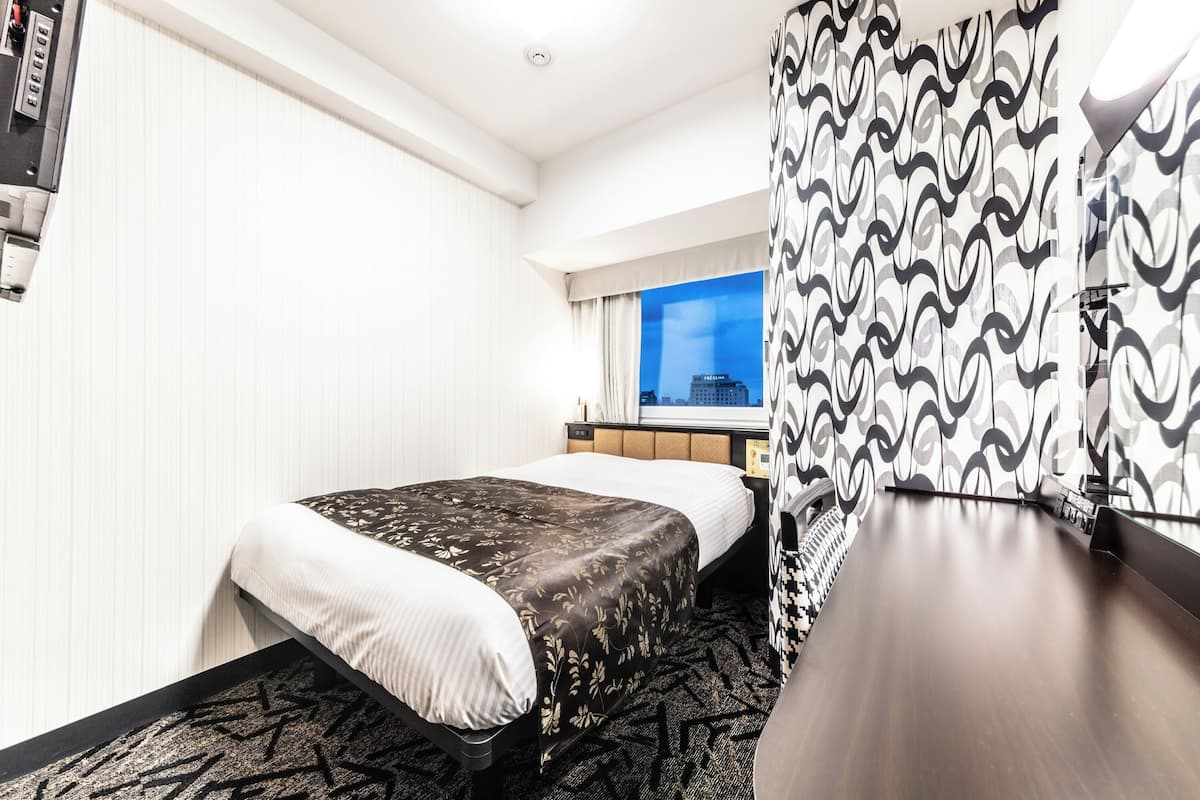 A hotel room with a bed, bedside table, and a desk with a chair.