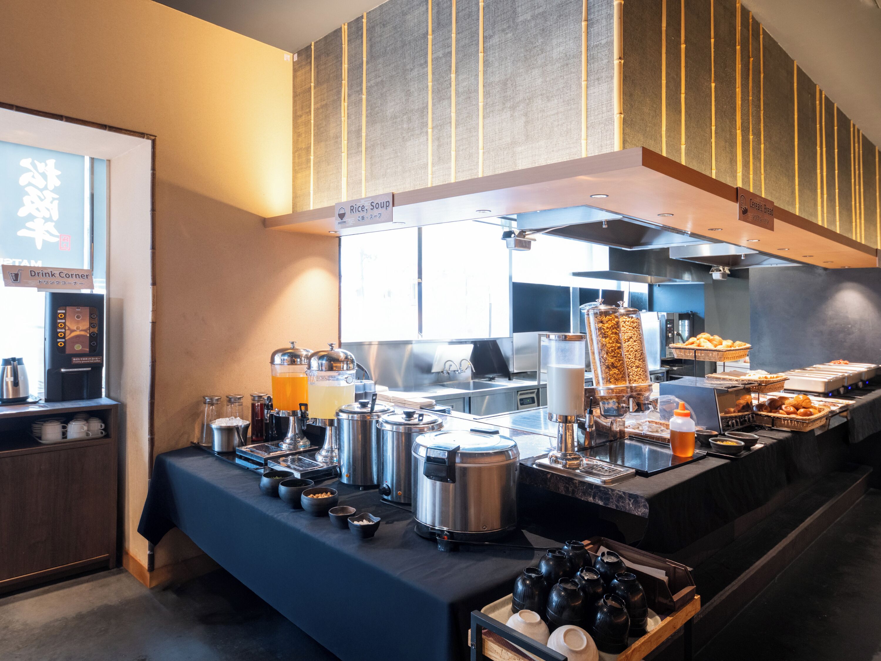 A buffet setup with various food and drink dispensers, a coffee machine, and a sign indicating a drink corner.