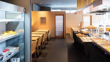 A buffet area with various food items, a long table with chairs, and a glass display case with condiments.