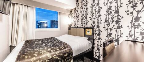 A hotel room with a bed, a desk, a view of the cityscape through the window, and a wall with a floral pattern.