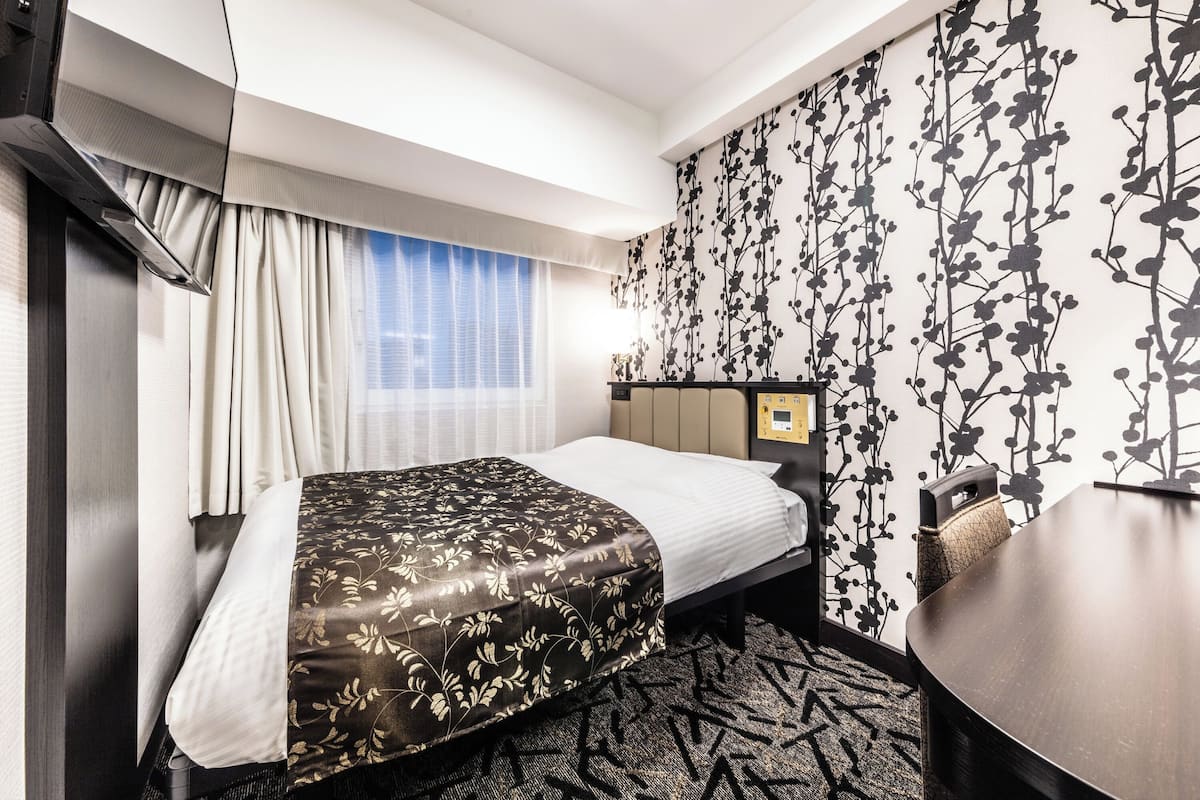 A hotel room with a bed, a desk, and a window with curtains.