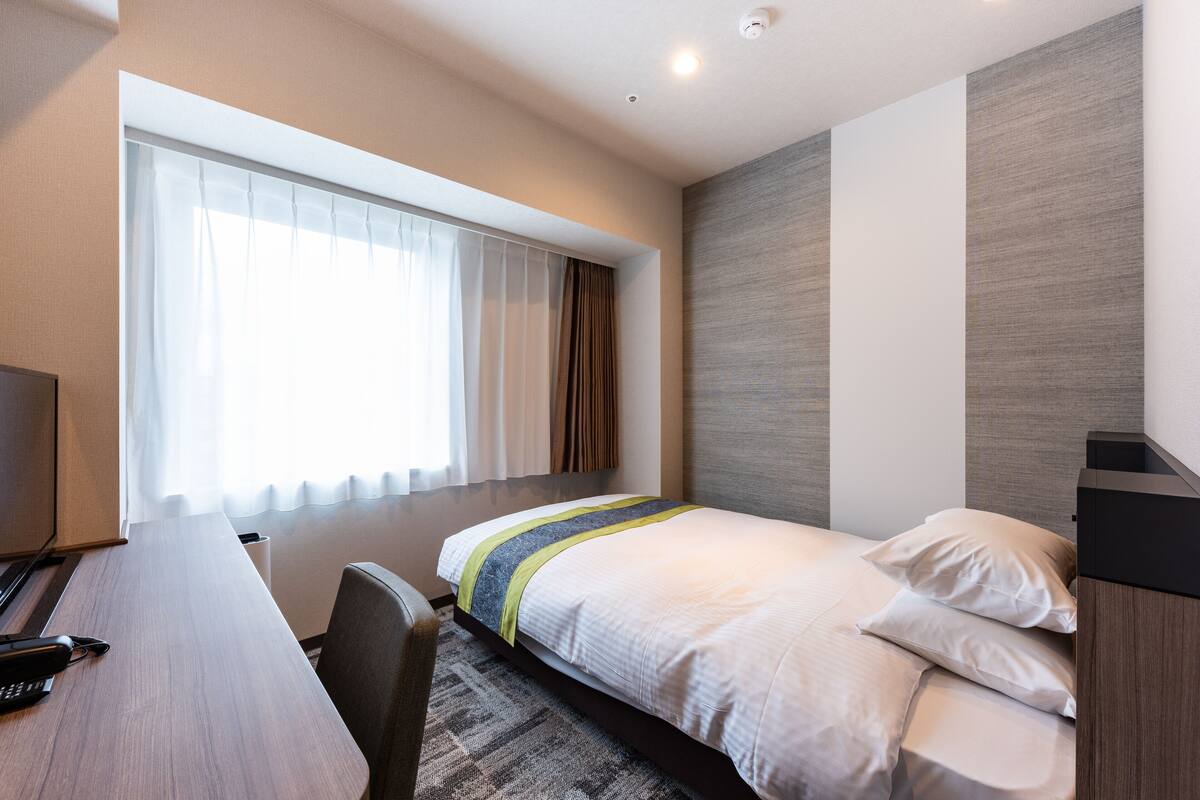 A hotel room with a bed, a desk, and a window with curtains.