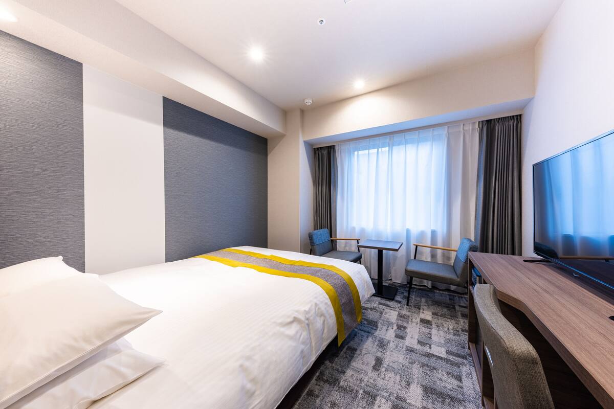 A hotel room with a bed, a desk, a chair, and a TV.