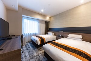 Quarto de hotel com duas camas, uma escrivaninha, uma televisão e uma janela com cortinas.