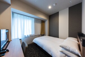 A hotel room with a bed, a desk with a computer, and a window with curtains.