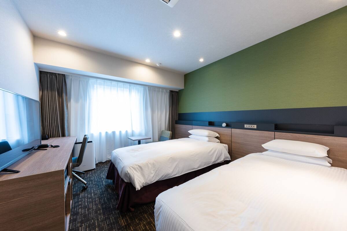 A hotel room with two beds, a desk, and a chair.