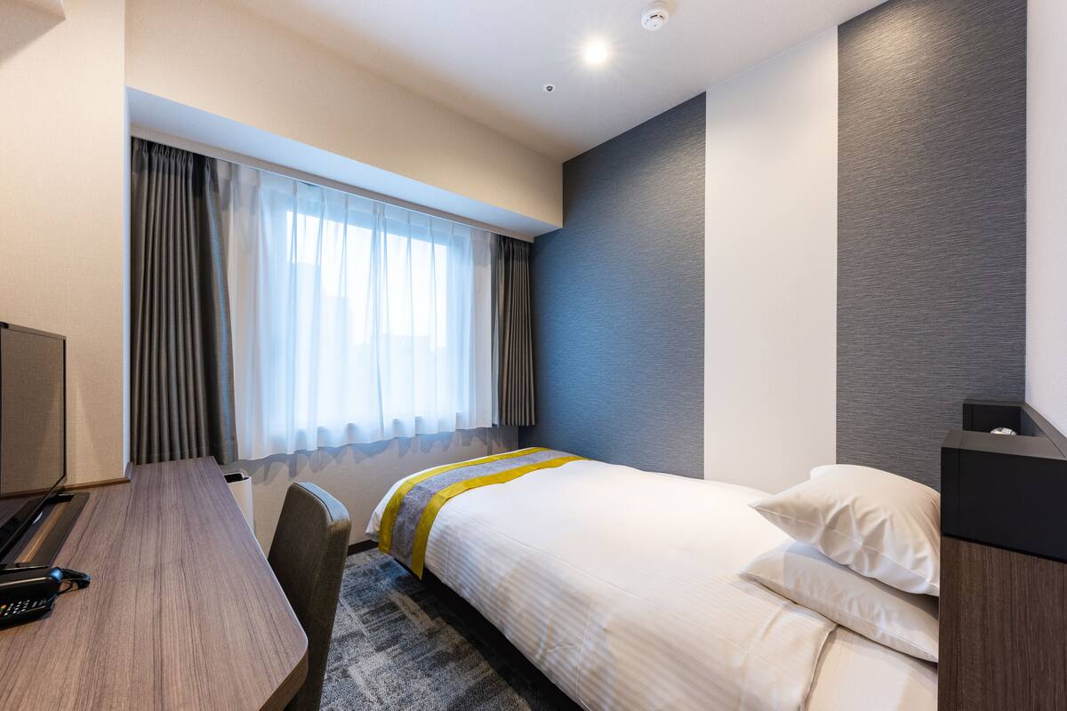 A hotel room with a bed, a desk, a chair, and a window with curtains.