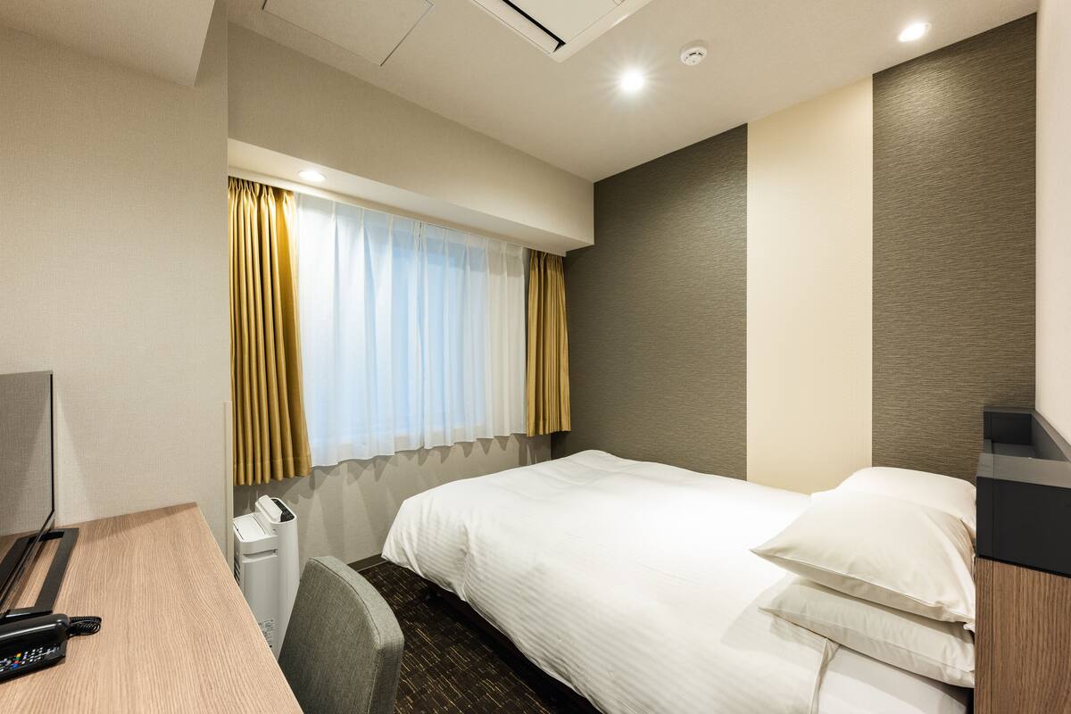 A hotel room with a bed, a desk with a telephone, and a chair.