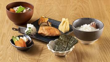 A wooden table with various Japanese dishes including a bowl of soup, a plate with fish, rice, and seaweed.