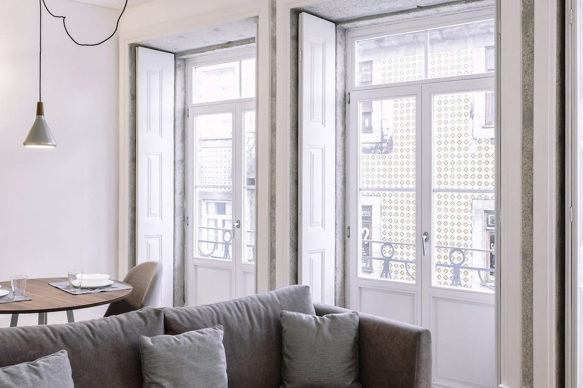 Un salón moderno con un sofá gris, una mesa de comedor redonda y ventanas amplias con vistas a la ciudad.
