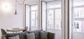 A modern living room with a grey sofa, a round dining table, and large windows with a view of the city. -  ORM - 3 C´s Apartments (Porto)