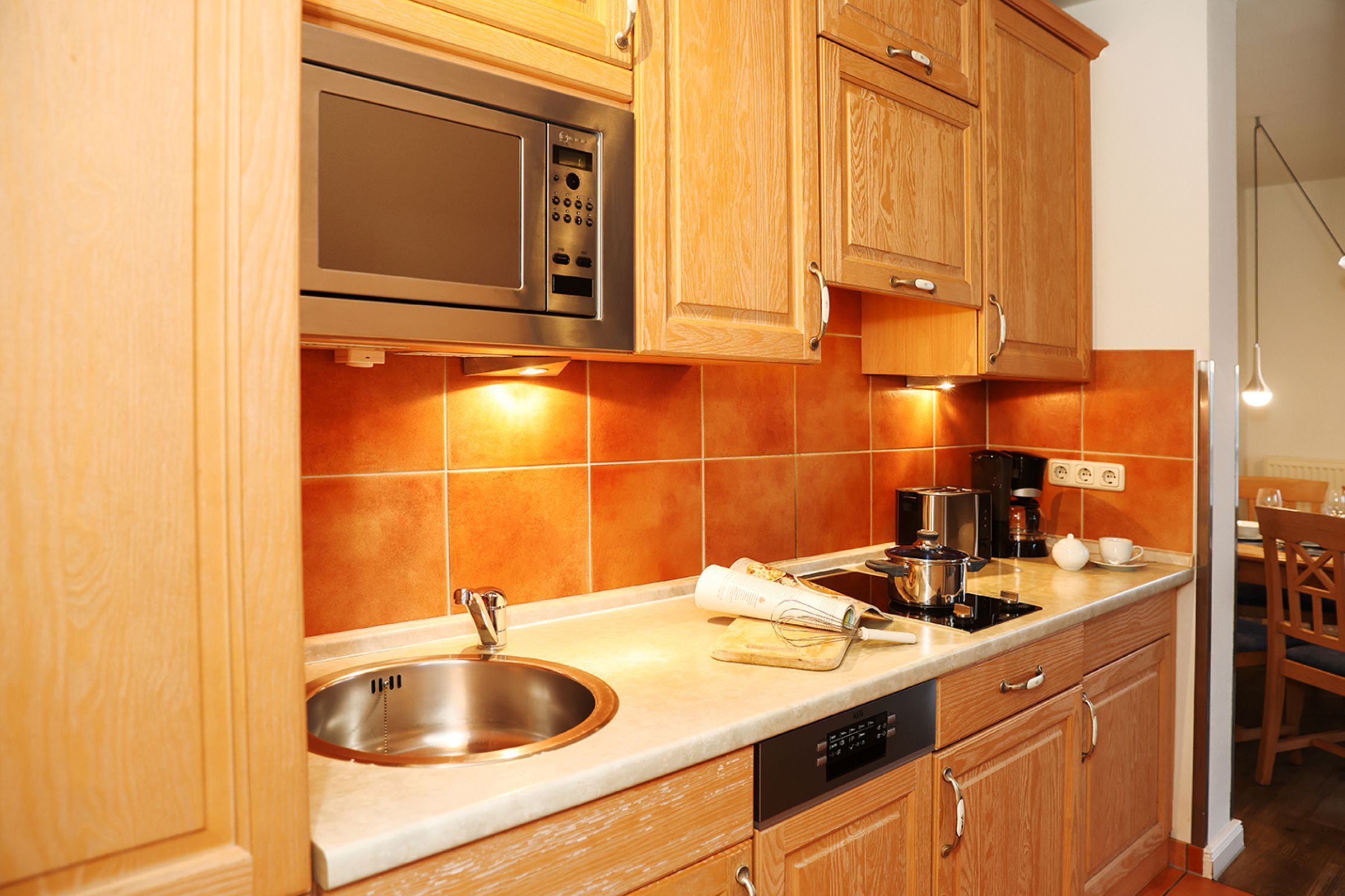 Una cocina con armarios de madera, un lavamanos de acero inoxidable, un microondas y una cafetera.