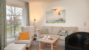 A living room with a sofa, armchair, ottoman, coffee table, and a painting of a lighthouse.