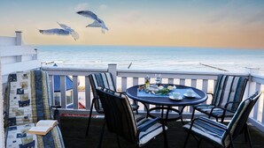 En terrasse med et bord og stole, med udsigt over havet, og måger i baggrunden.