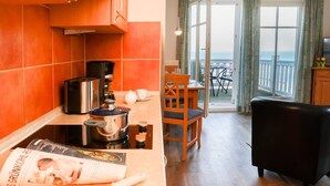 A kitchen with orange tiles, a stove, and a dining area with a chair and table.
