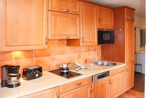 A kitchen with wooden cabinets, a microwave, a coffee maker, a toaster, a sink, and a dishwashing unit. - Meeresblick House WM416 - WM416 (Kühlungsborn)