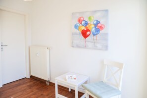 A room with a white radiator, a white chair with a cushion, and a painting of balloons on the wall.